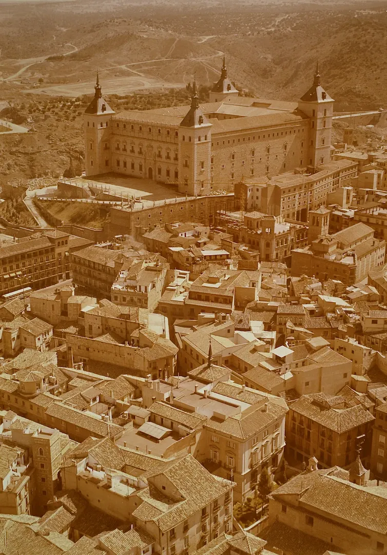 Vista aérea de la ciudad de Toledo, con el Alcázar al fondo. En la parte inferior de la imagen, el edificio de la sucursal del Banco de España (calle Nueva, sede entre 1954 y 2011, obra del arquitecto Luis Menéndez Pidal). 1976. Fotógrafo: Paisajes Españoles. Positivo. Copia cromógena. N.º inv. 15065.