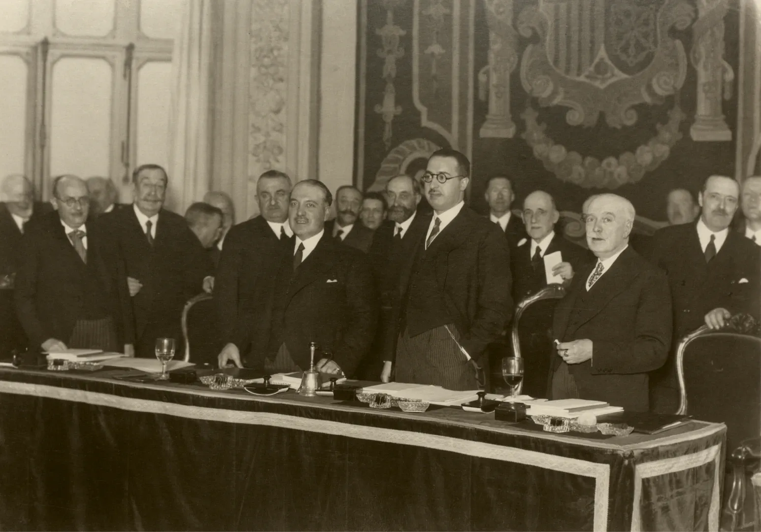 Reunión de la Junta General de Accionistas celebrada los días 4 y 11 de marzo de 1934. Los miembros del Consejo de Gobierno, detrás de la mesa presidencial. En primer plano, de izquierda a derecha, Pedro Pan Gómez, subgobernador 1.º; Alfredo Zavala Lafora, gobernador, y José Suárez-Figueroa, subgobernador 2.º. En segundo término, entre otros, los consejeros José González Pintado Hermoso, Francisco Aritio Gómez, José Varela de Limia y Lorenzo Martínez Fresneda Jouvé. Fotógrafo: Cristóbal Portillo Robles. Positivo. Plata en gelatina. N.º inv. 2134.