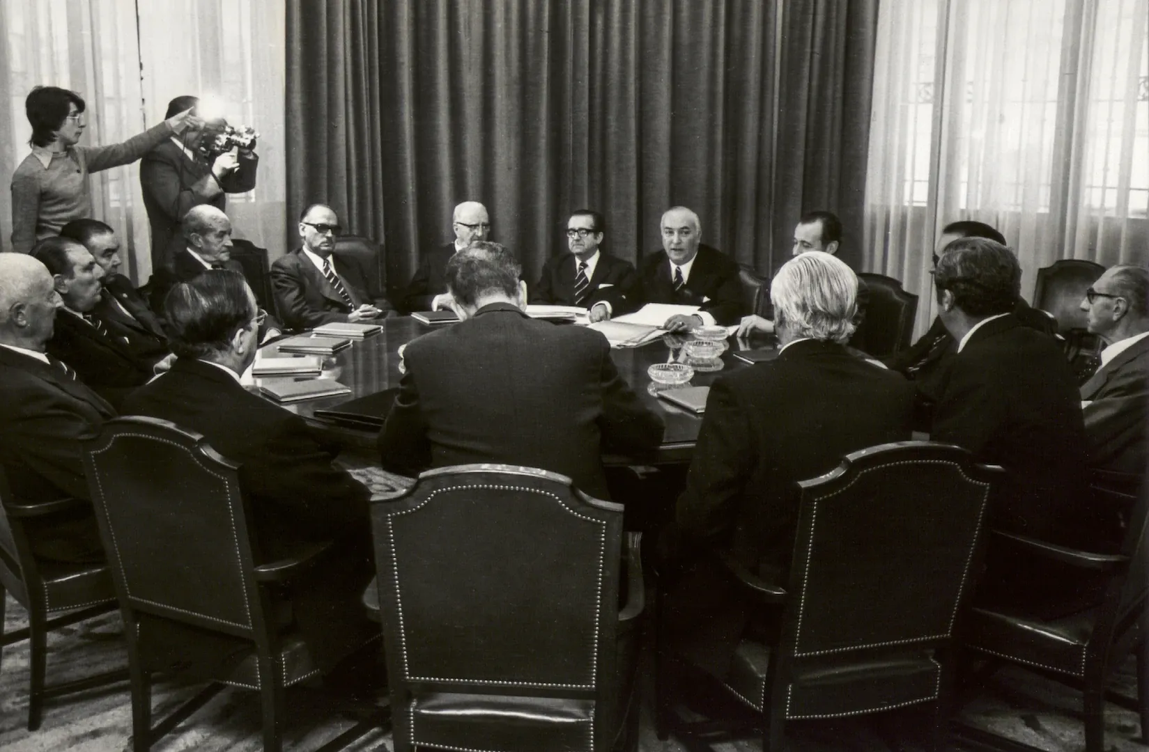 Reunión del Consejo General del Banco de España en la sucursal de Valencia. En el centro de la fotografía, Luis Coronel de Palma, gobernador; a su derecha, José María Latorre Segura, subgobernador 1.º; a su izquierda, Nemesio Fernández Cuesta, subgobernador 2.º. Se reconoce, entre otros, a los consejeros Alfonso Escámez, Julio Dánvila y Enrique Fuentes Quintana, al director general Juan Caldés Lizana y a Mariano Sebastián Herrador, secretario general. 16 de noviembre de 1973. Fotógrafo: Luis Vidal. Plata en gelatina. N.º inv. 4989.