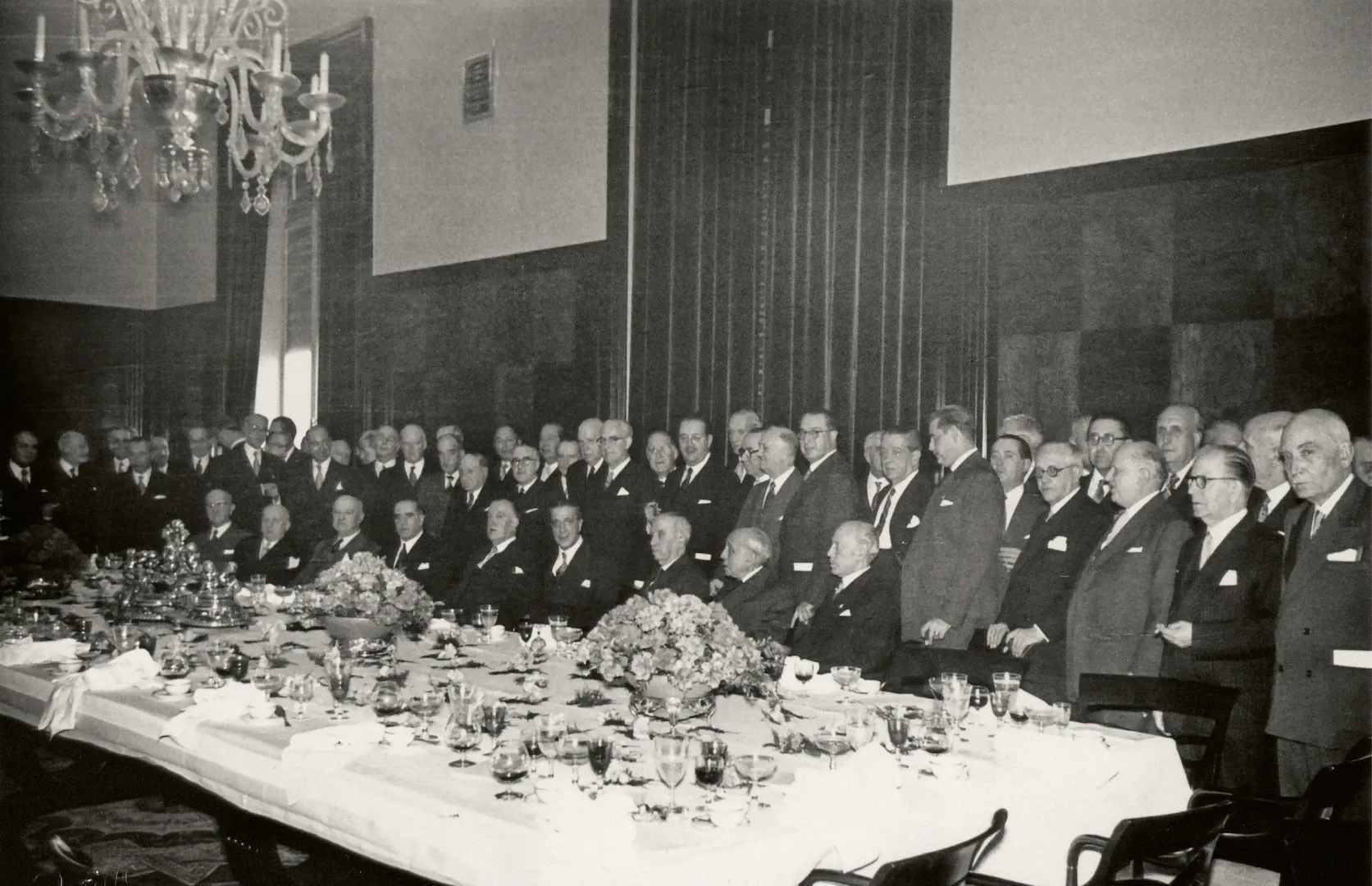 Actos de celebración del centenario del Banco de España, creado por la Ley de 28 de enero de 1856. Banquete ofrecido en el comedor de gala del Banco de España a las personalidades invitadas. En el centro de la fotografía, sentados, entre otros, Fernando Suárez de Tangil, ministro de Obras Públicas y consejero del Banco de España; Francisco Gómez del Llano, ministro de Hacienda, y Joaquín Benjumea, gobernador. De pie, entre otros, Luis Sáez de Ibarra, subgobernador; José Larraz, exministro de Hacienda, y Alfredo Zavala Lafora, exgobernador. 1956. Fotógrafo: Cristóbal Portillo Robles. Positivo. Plata en gelatina. N.º inv. 5432.