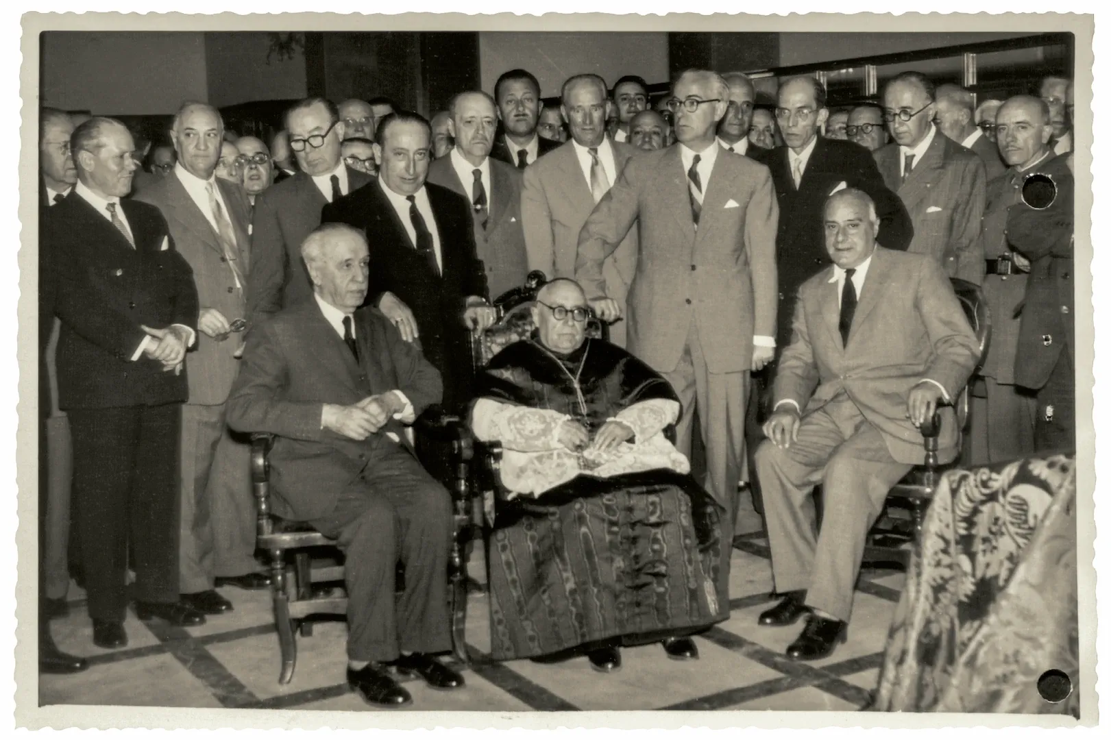 Sucursal de Toledo. Inauguración oficial del nuevo edificio en la confluencia de las calles Nueva y Cadenas, con asistencia de autoridades civiles y militares. En el centro, sentado, el cardenal arzobispo primado de Toledo, Enrique Pla y Deniel. A su derecha, el gobernador del Banco de España, Joaquín Benjumea Burín. A su izquierda, el gobernador civil de Toledo, Andrés Marín Martín. 6 de julio de 1954. Fotógrafo: Fotografía Rodríguez. Positivo. Plata en gelatina. N.º inv. 7597.