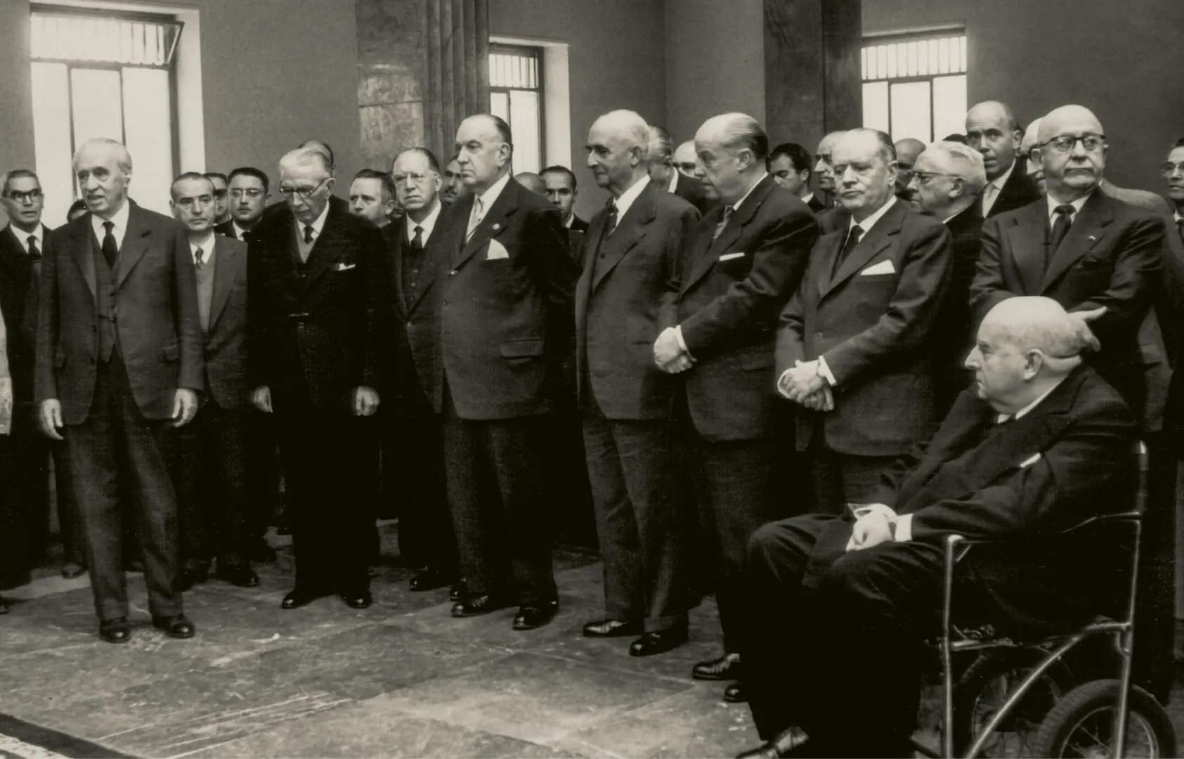 Sucursal de Burgos. Acto de inauguración del edificio, con presencia del gobernador del Banco de España, Joaquín Benjumea Burín (de pie, a la izquierda de la fotografía), el gobernador civil de Burgos, Servando Fernández-Victorio (de pie, tercero por la derecha), y miembros de la alta administración del Banco (calle de Vitoria, 34, sede entre 1959 y 2003, obra del arquitecto José Yárnoz Larrosa). 24 de octubre de 1959. Fotógrafo: Eliseo Villafranca Hernando. Positivo. Plata en gelatina. N.º inv. 11798.