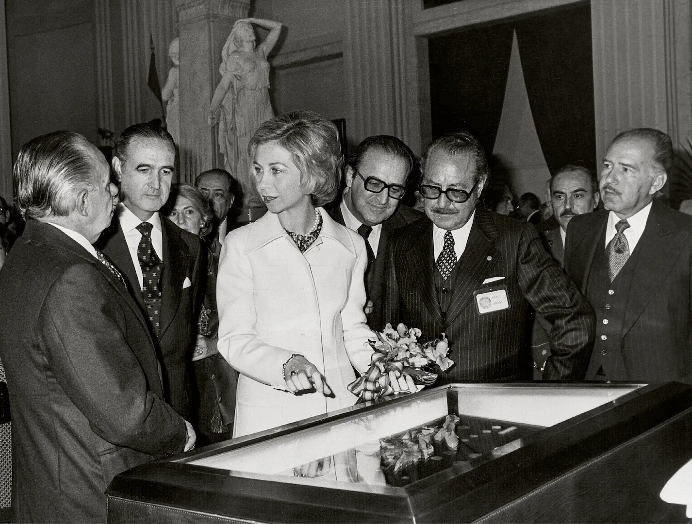 Inauguración de la Exposición Numismática del Banco de México en la sede del Banco de España, en Madrid. En el centro de la fotografía, la reina doña Sofía, que aparece acompañada, entre otros, por José M.ª López de Letona, gobernador del Banco de España, Enrique Fuentes Quintana, vicepresidente del Gobierno para Asuntos Económicos, y Gustavo Romero, director general del Banco de México. 1978. Fotógrafo: Europa Press. Positivo. Plata en gelatina.