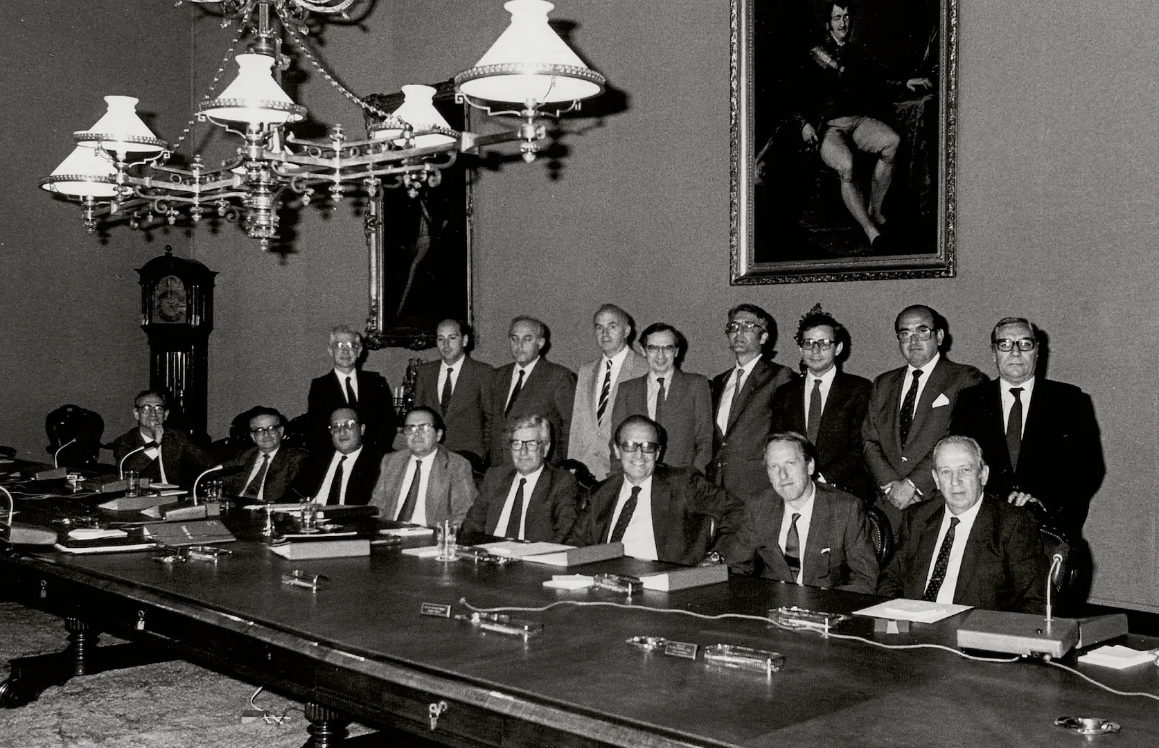 Reunión del Consejo General del Banco de España. De izquierda a derecha, sentados: Aristóbulo de Juan de Frutos, Luis Ángel Rojo, directores generales; Rafael de la Cruz Corcoll, director general de Presupuestos; Juan Antonio Ruiz de Alda, subgobernador; Mariano Rubio, gobernador; Enrique Fuentes Quintana, Tomás Ramón Fernández Rodríguez y Manuel Olivencia, consejeros. De pie: Enrique Giménez-Arnau, secretario general; Luis Ibáñez, representante de Personal; José Luis Sureda, Gonzalo Anes, consejeros; Raimundo Ortega, director general; José María García Alonso, director general del Tesoro y Política Financiera; Carlos Bustelo, consejero; Ángel Madroñero y Antonio Sánchez-Pedreño, directores generales. 17 de junio de 1986. Positivo. Plata en gelatina. Fotógrafo: desconocido.